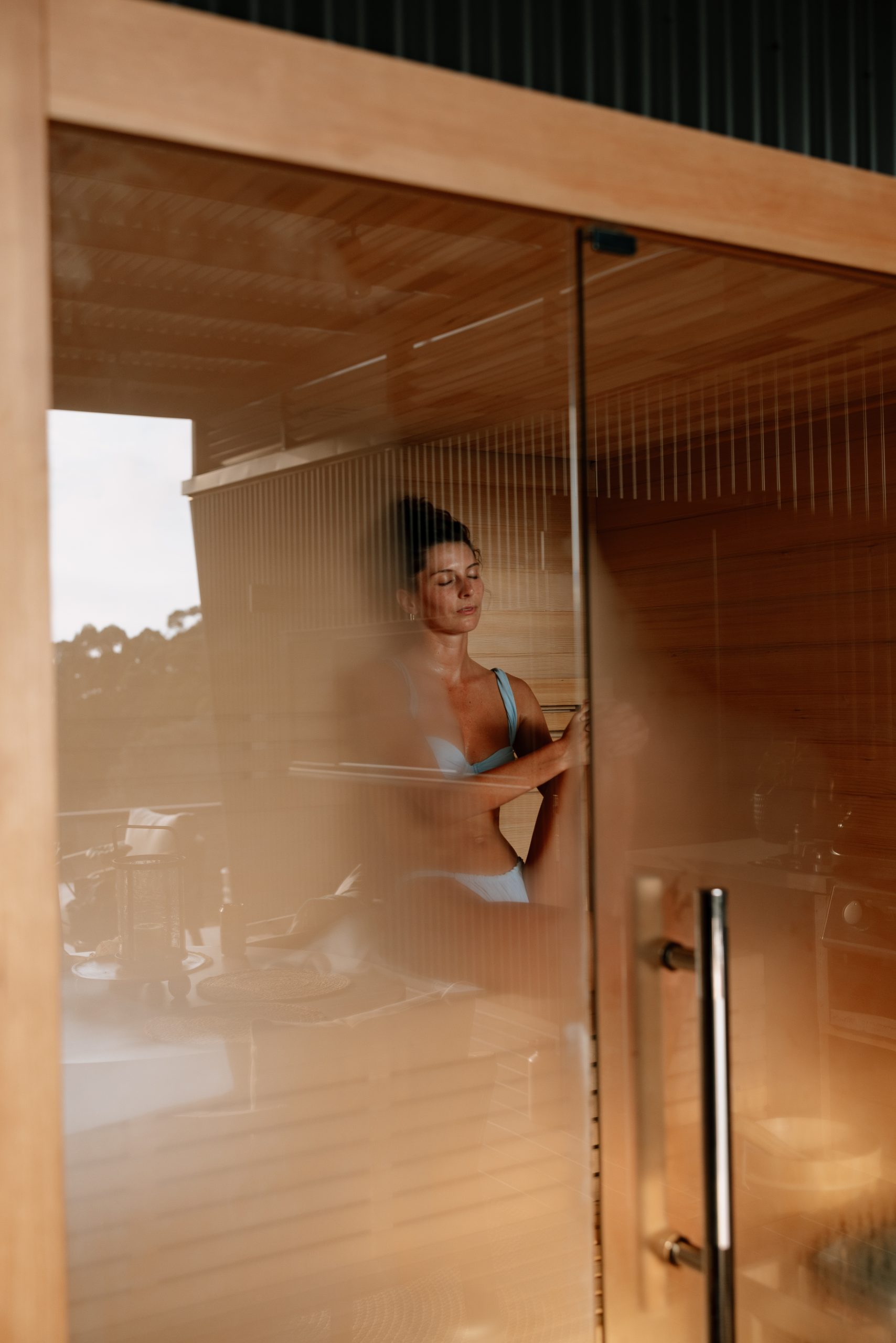 Woman relaxing in sauna inside two-bedroom cabin in Denmark WA with timber interior and steam