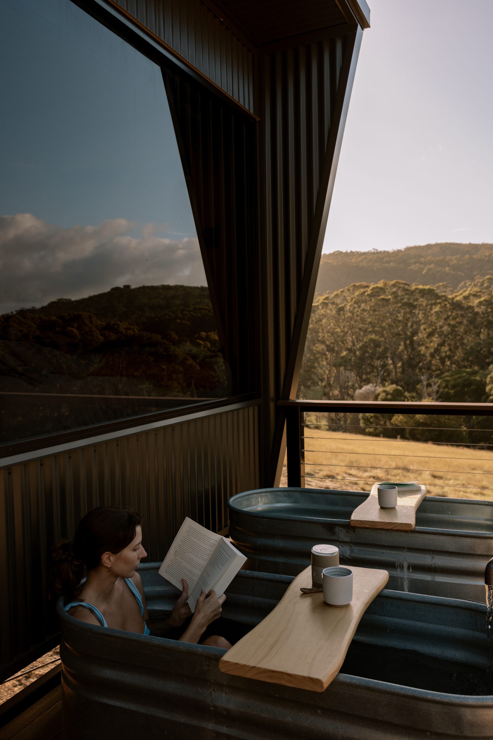 Woman reading a book in outdoor twin baths at two-bedroom cabin in Denmark WA surrounded by nature